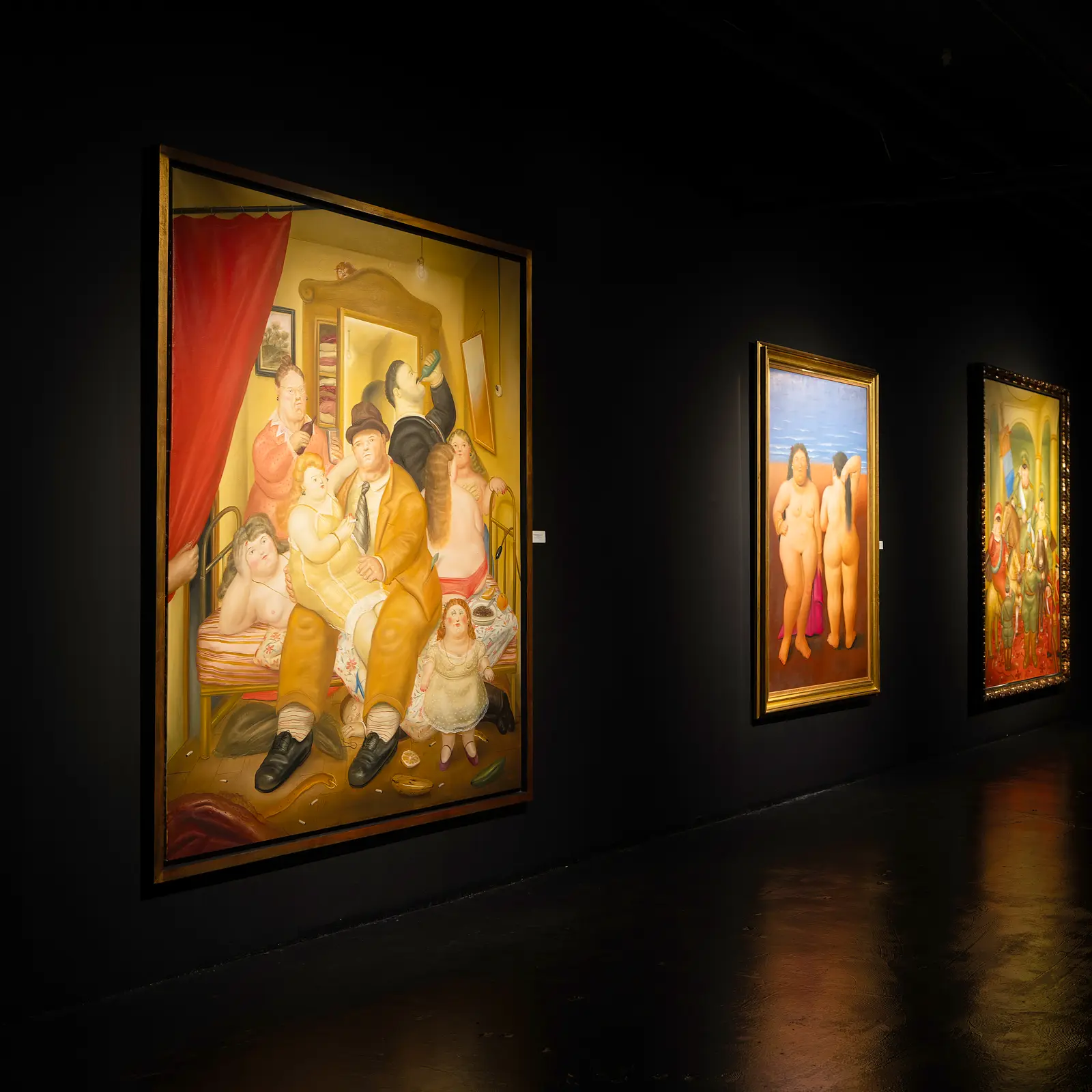 Installation view of Masters of the Museum at Nader Museum, with paintings by Fernando Botero and other Latin American masters illuminated against black gallery walls.