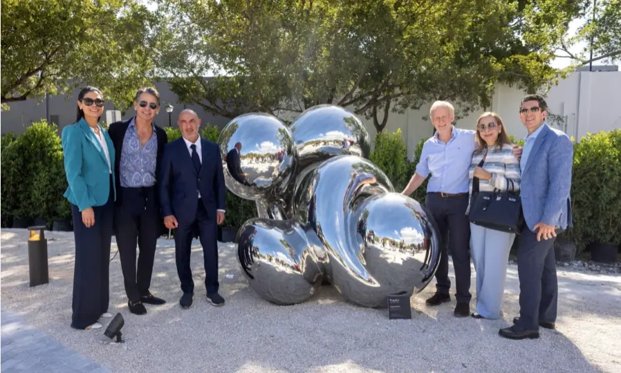 Opening guests beside a polished, reflective sculpture at Nader Sculpture Park.